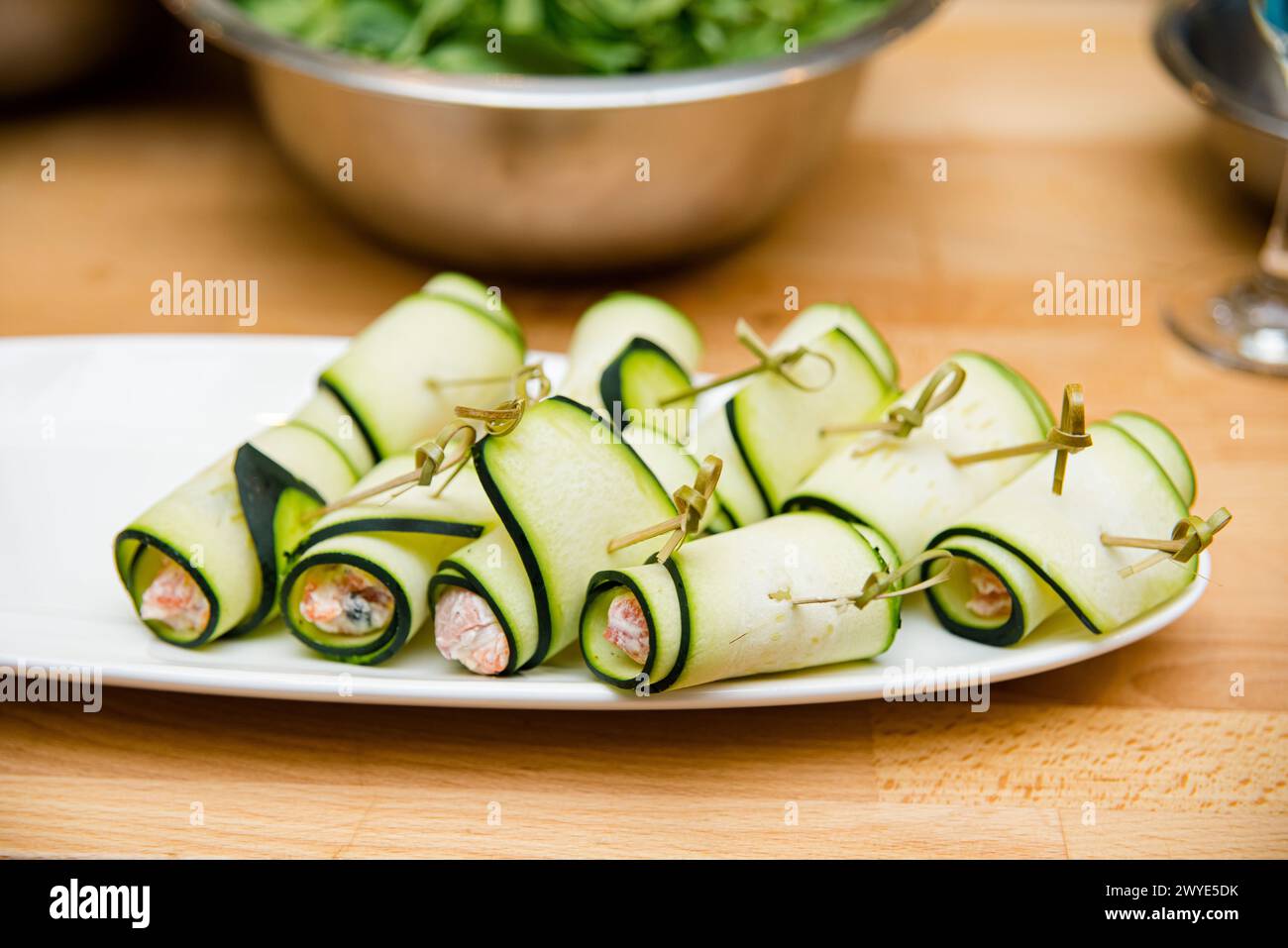 Rouleaux de courgettes fraîches remplis de saumon fumé et de fromage à la crème, soigneusement disposés sur un plat blanc pour un apéritif. Banque D'Images