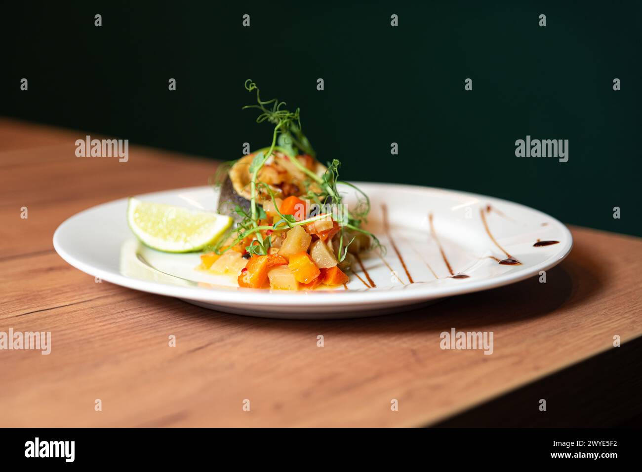 Élégant placage de poisson poêlé garni de pousses de pois, servi avec des légumes coupés en dés et une tranche de citron vert, garni de glaçage balsamique. Banque D'Images