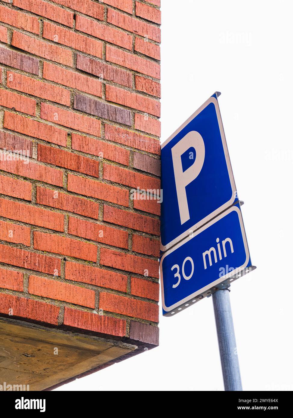Un panneau de stationnement bleu est affiché bien en évidence à côté d'un bâtiment en briques rouges dans un cadre urbain. Le panneau indique les réglementations et restrictions de stationnement Banque D'Images