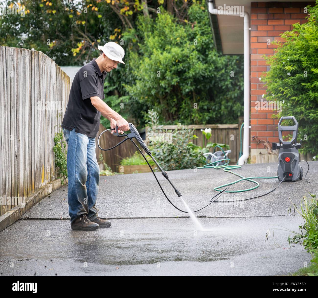 Homme nettoyant l'allée en béton à l'aide d'un nettoyeur haute pression. Banque D'Images