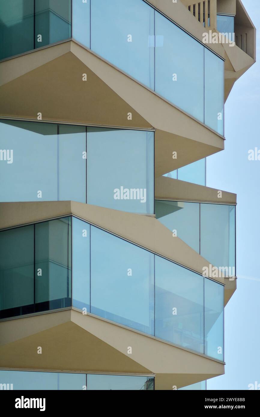 Gros plan d'un bâtiment à Tarragone, avec des balcons en verre qui reflètent le ciel catalan, mettant en valeur l'innovation et le style de vie urbain moderne. Banque D'Images