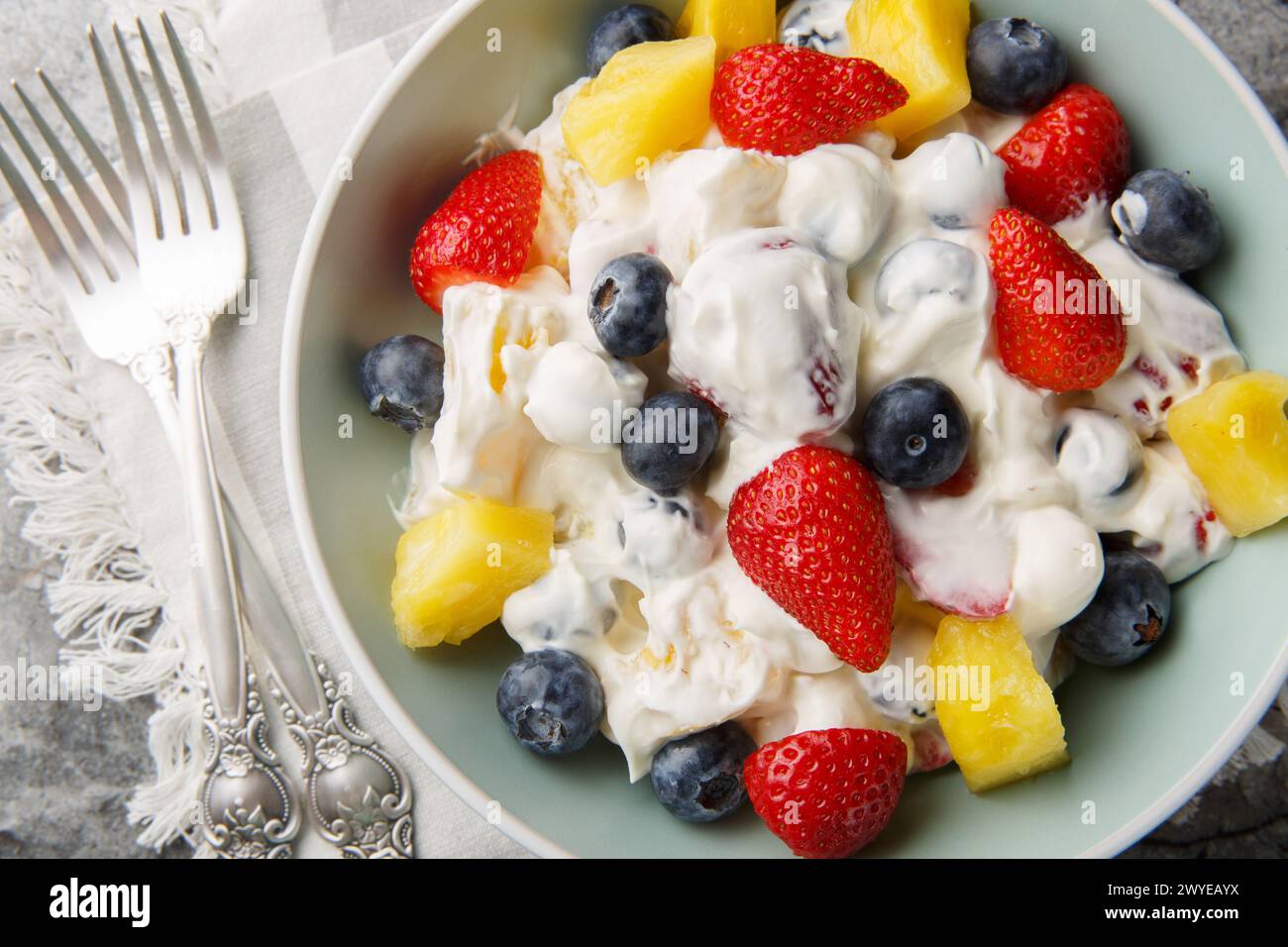 Salade de cheesecake d'été avec fraises, bleuets, ananas, habillé de fromage à la crème et de crème gros plan dans un bol sur une table en marbre. HORIZONTA Banque D'Images