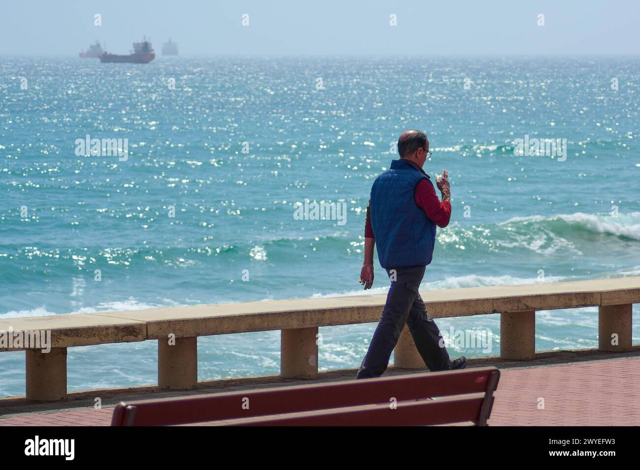 Tarragone, Espagne - 6 avril 2024 : un marcheur solitaire profite d'une promenade paisible sur le front de mer de Tarragone, avec la mer bleue étincelante et un bateau dans le distan Banque D'Images