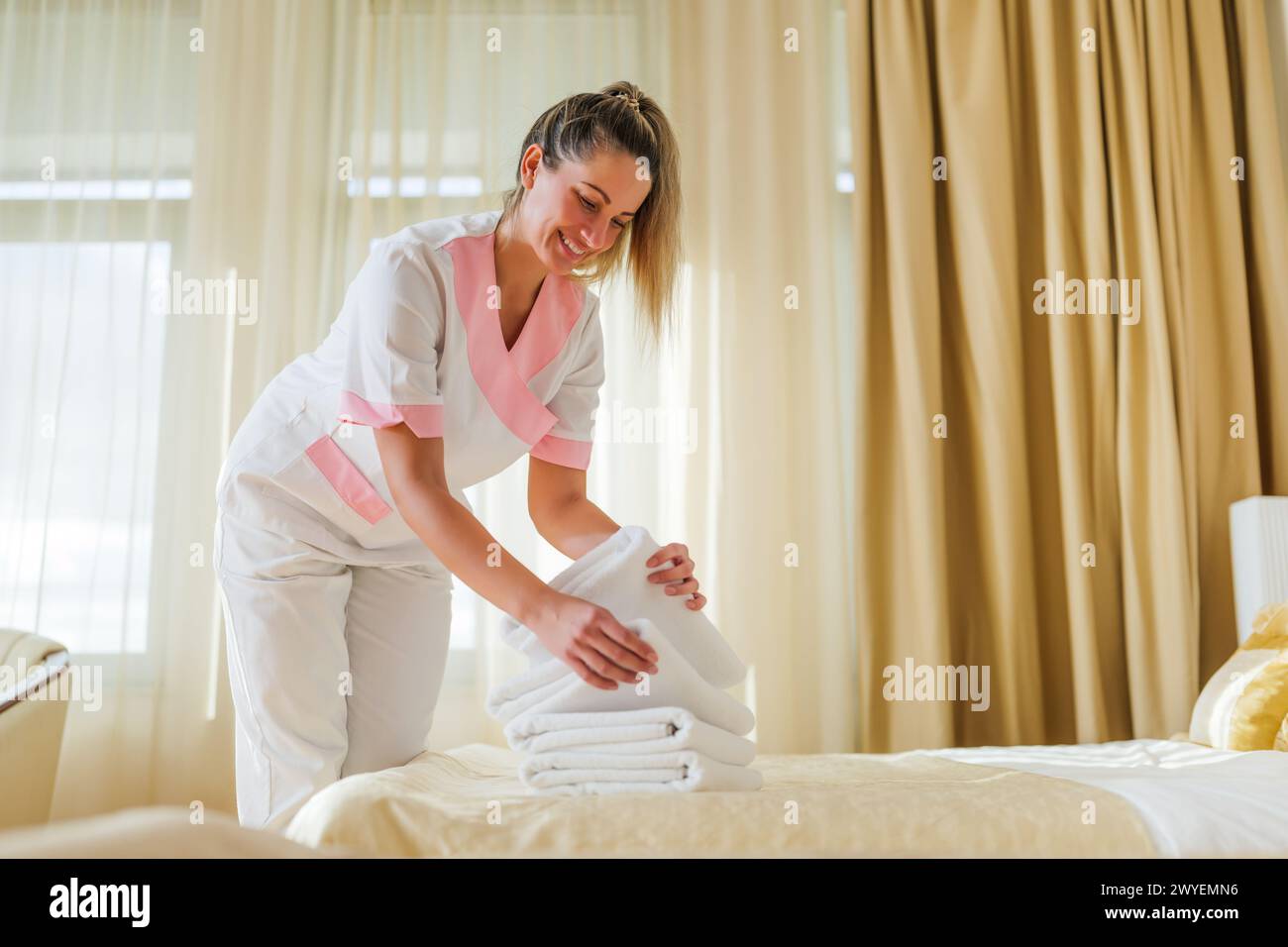 Belle femme de chambre mettant des serviettes propres et propres sur le lit de la chambre. Banque D'Images
