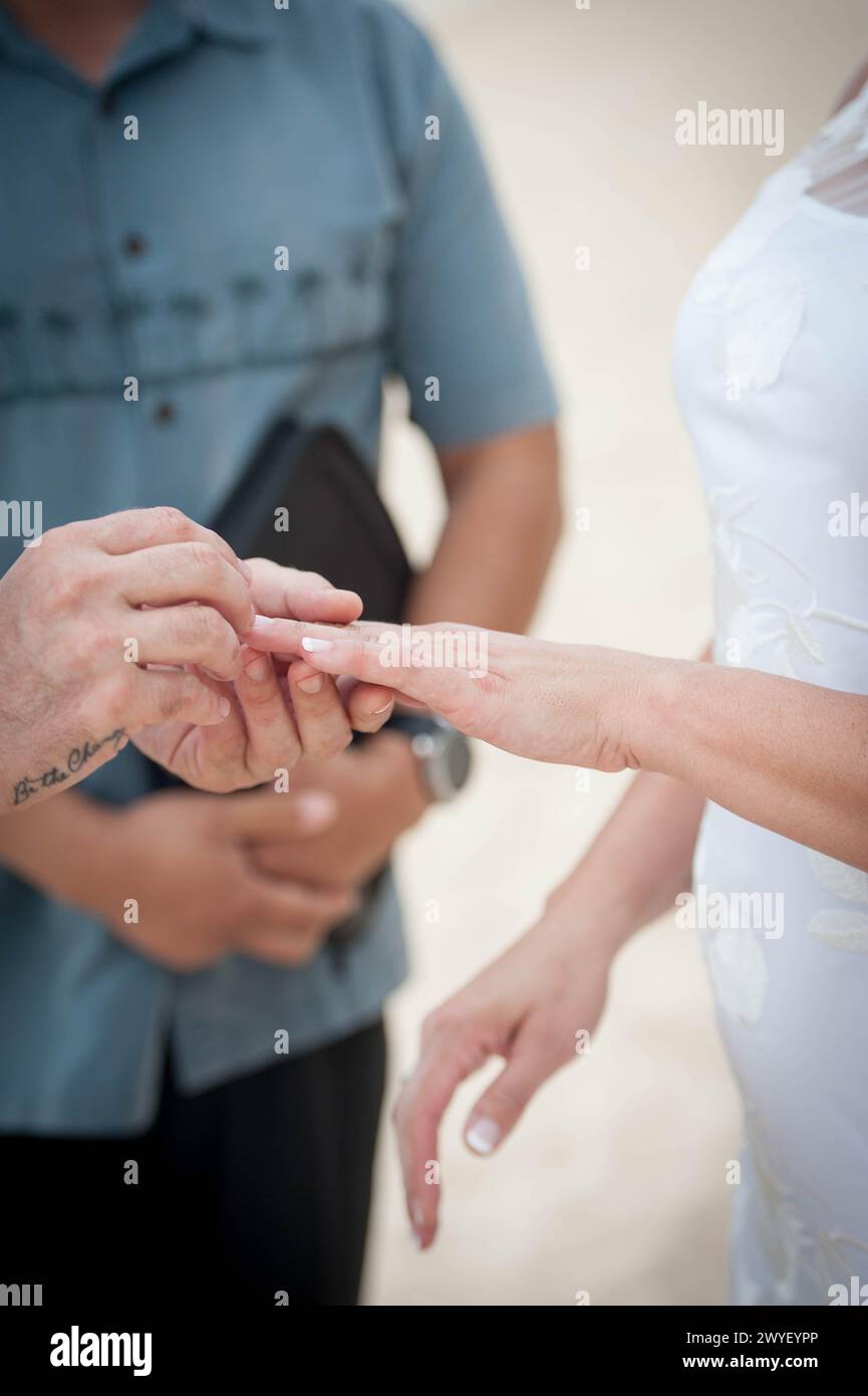 Sur une côte hawaïenne ensoleillée, un marié place une bague sur sa mariée leurs vœux murmurmurés avec le murmure de la mer leur avenir aussi brillant que le soleil tropical. Banque D'Images