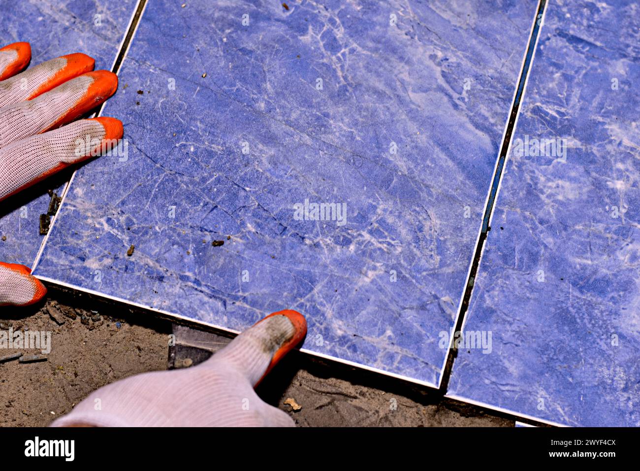 Gros plan des mains de l'homme, vêtues de mitaines, dans l'une desquelles il voit une spatule, avec laquelle il déchire les carreaux de céramique du sol. Banque D'Images