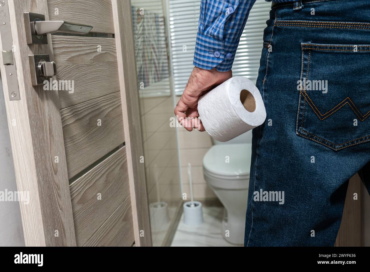 La main d'un homme plus âgé tenant un rouleau de papier toilette devant les toilettes. Banque D'Images