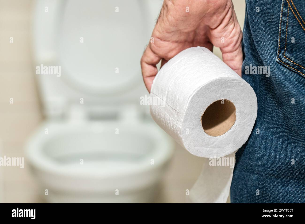 La main d'un homme plus âgé tenant un rouleau de papier toilette devant les toilettes. Banque D'Images