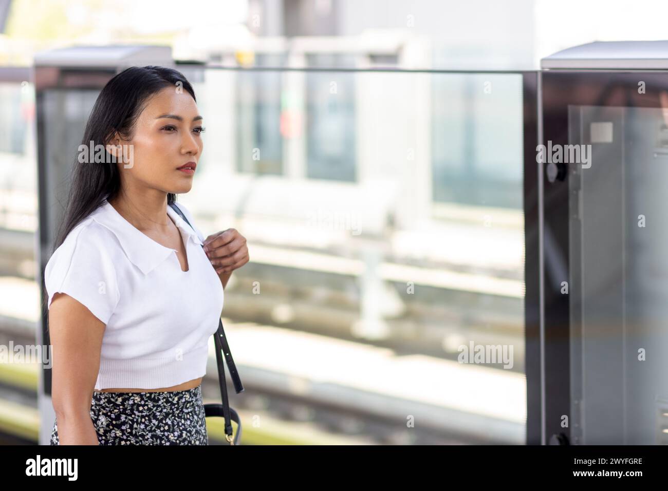 Jeune femme attendant un train sur un quai avec une barrière de protection Banque D'Images