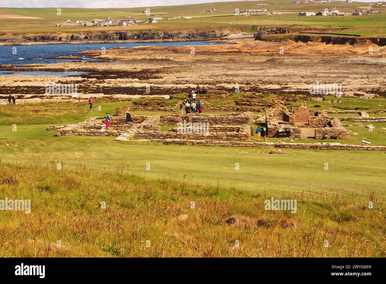 Visiteurs visitant la colonie nordique sur le Brough de Birsay, Orcades, Écosse Royaume-Uni avec la chaussée vers le continent et le Earl's Palace Banque D'Images