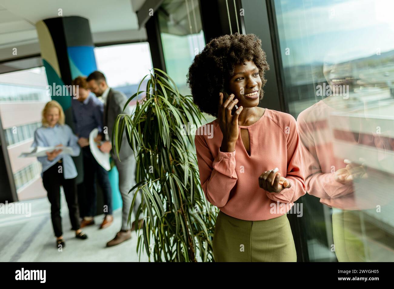 Femme afro-américaine sourit tout en parlant au téléphone au milieu de collègues dans un cadre de bureau, exsudant professionnalisme et joie. Banque D'Images