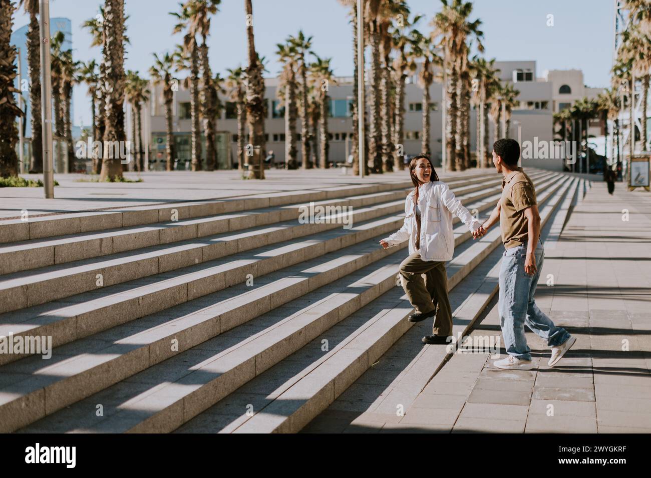 Les jeunes couples se réunissent joyeusement sur les marches d'une promenade bordée de palmiers dans le paysage urbain animé de Barcelonas Banque D'Images