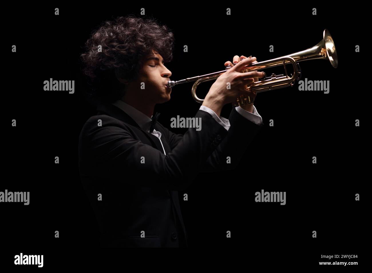Plan de profil d'un jeune homme jouant de la trompette isolé sur fond noir Banque D'Images