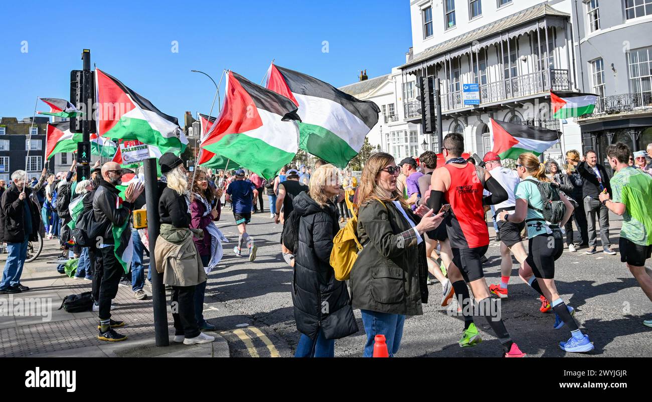 Brighton UK 7 avril 2024 - les manifestants Pro Palestine brandissent des drapeaux alors que des milliers de coureurs participent au marathon de Brighton par une journée ensoleillée mais venteuse : Credit Simon Dack / Alamy Live News Banque D'Images