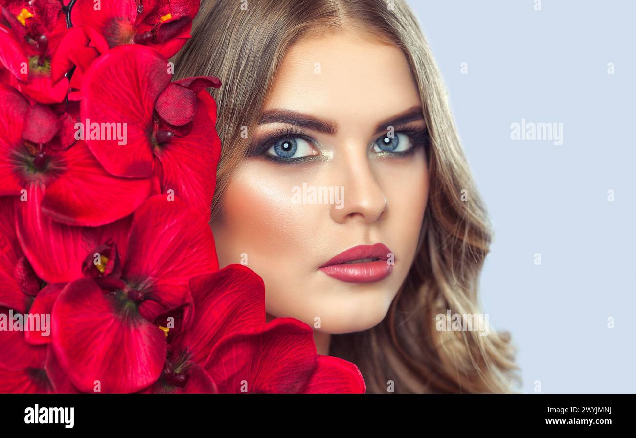 Portrait d'une femme avec un beau maquillage tient une orchidée rouge dans ses mains. Maquillage professionnel et soins de la peau. Banque D'Images