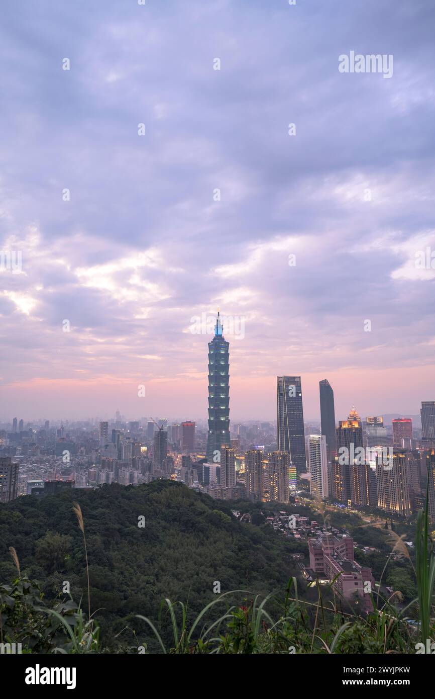 Une vue surélevée de la ville de Taipei au crépuscule avec des gratte-ciels contre un coucher de soleil subtil, prise d'une zone montagneuse avec du feuillage Banque D'Images