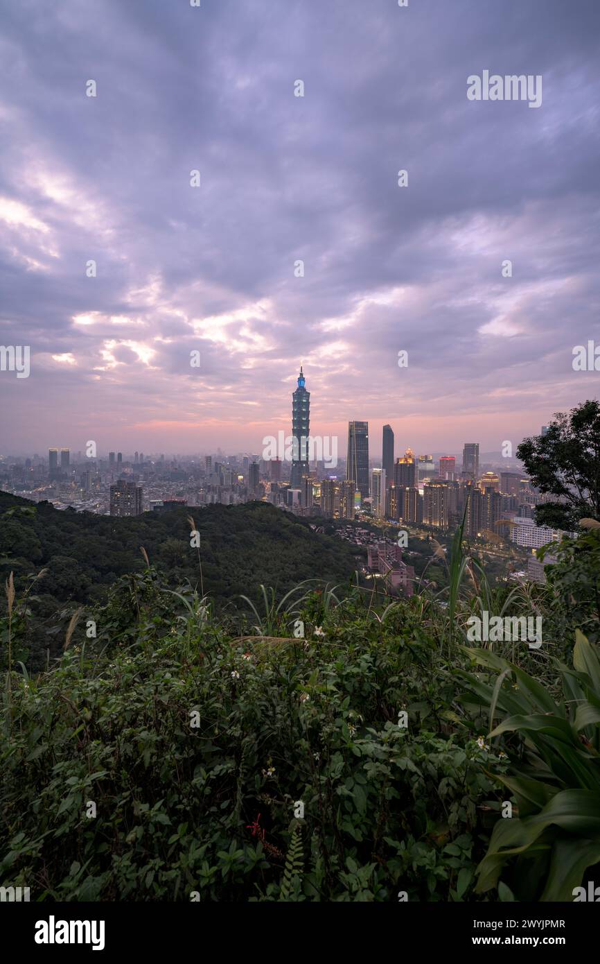 Une vue surélevée de la ville de Taipei au crépuscule avec des gratte-ciels contre un coucher de soleil subtil, prise d'une zone montagneuse avec du feuillage Banque D'Images