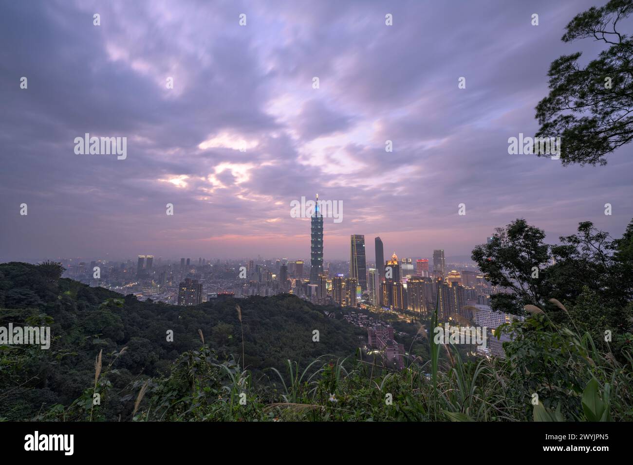 Une vue surélevée de la ville de Taipei au crépuscule avec des gratte-ciels contre un coucher de soleil subtil, prise d'une zone montagneuse avec du feuillage Banque D'Images