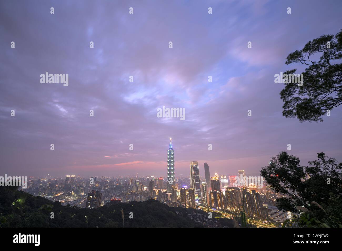 Une vue surélevée de la ville de Taipei au crépuscule avec des gratte-ciels contre un coucher de soleil subtil, prise d'une zone montagneuse avec du feuillage Banque D'Images