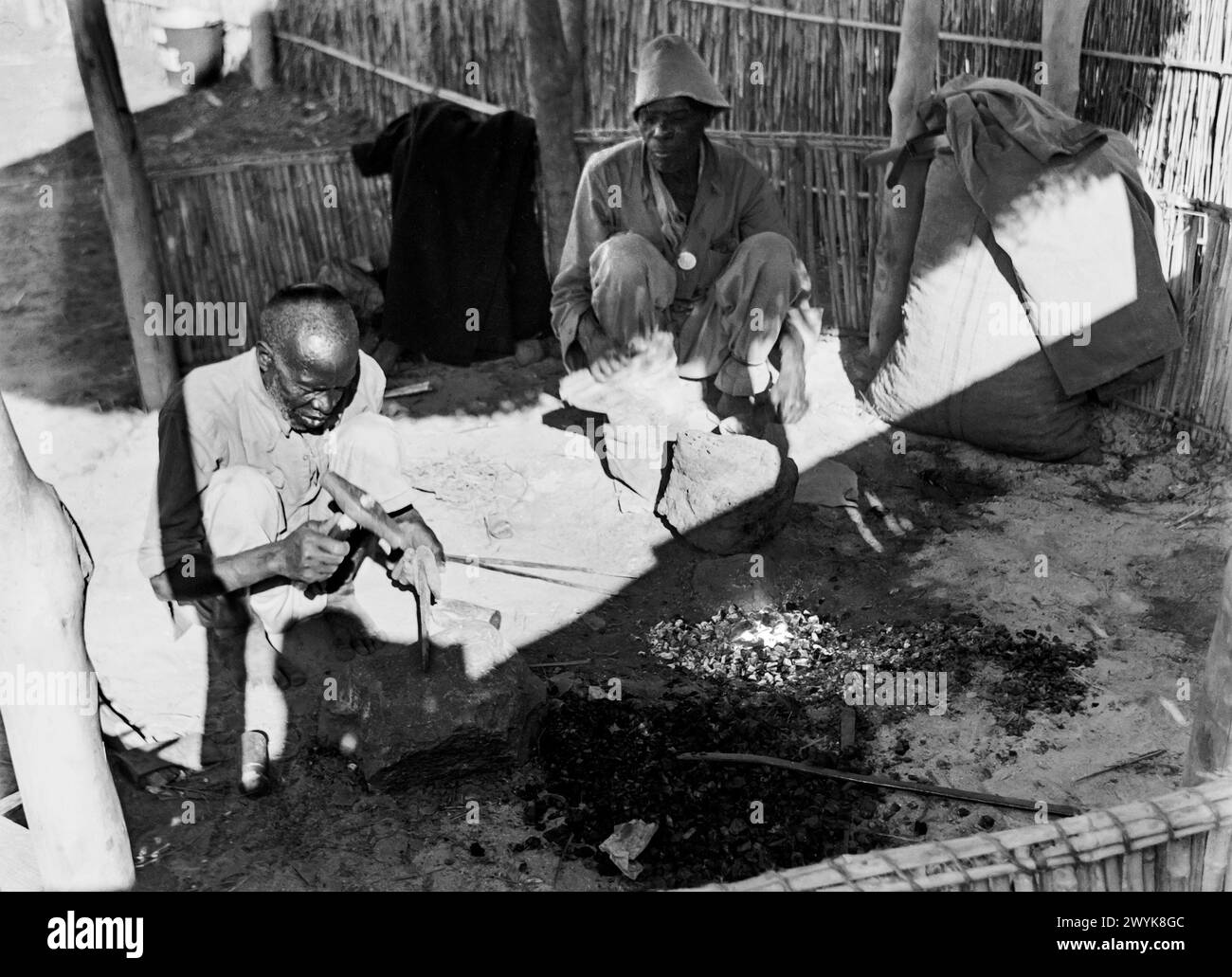 Forgerons travaillant avec un feu dans le sol alimenté par soufflet pompé à la main dans un village près de Ndola, Rhodésie du Nord (aujourd'hui Zambie) c1956 Banque D'Images