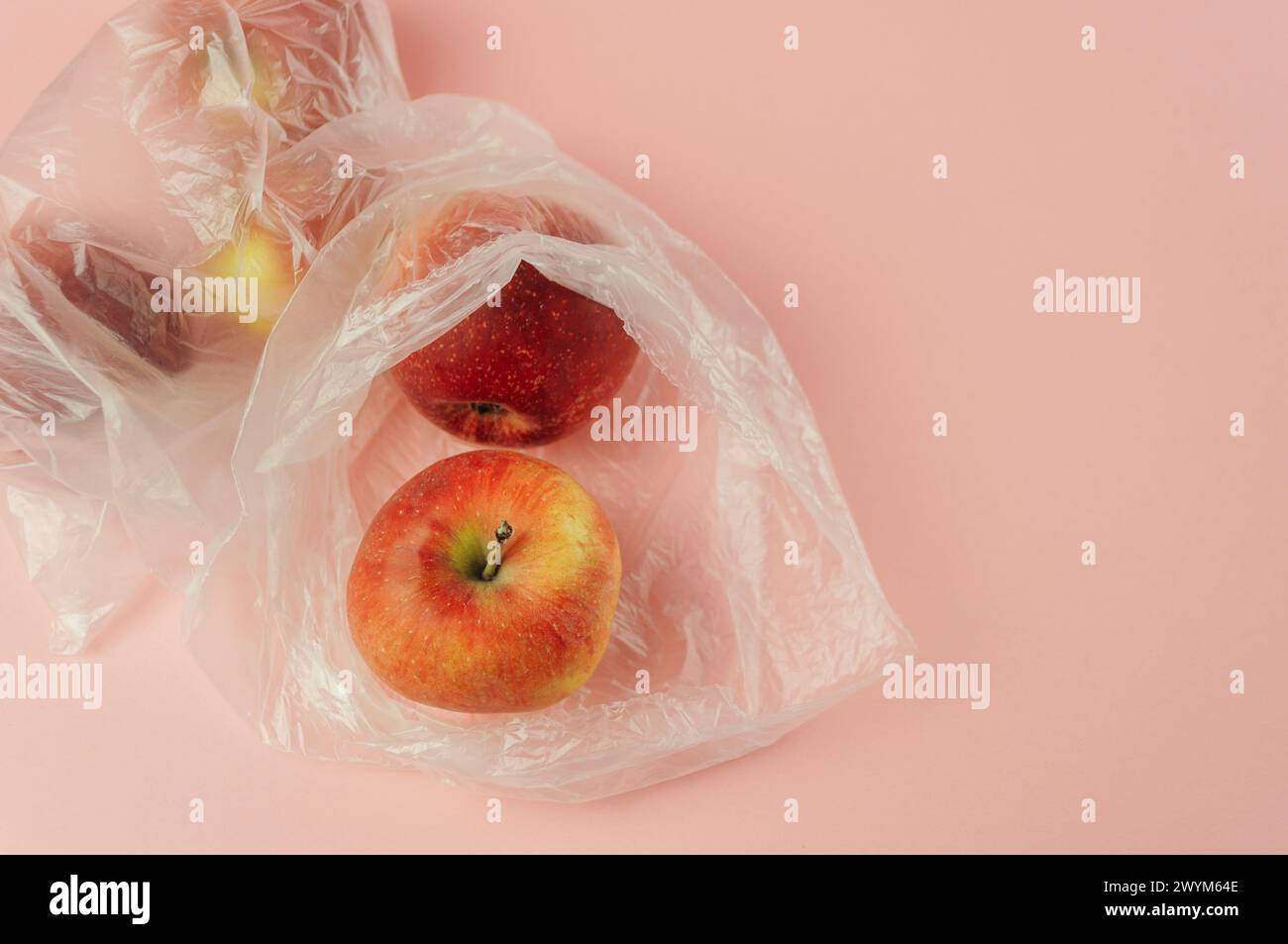 Un sac en plastique avec une pomme rouge à l'intérieur. Le sac est placé sur un fond rose. Concept de gaspillage et de préoccupation environnementale, comme le sac en plastique i Banque D'Images