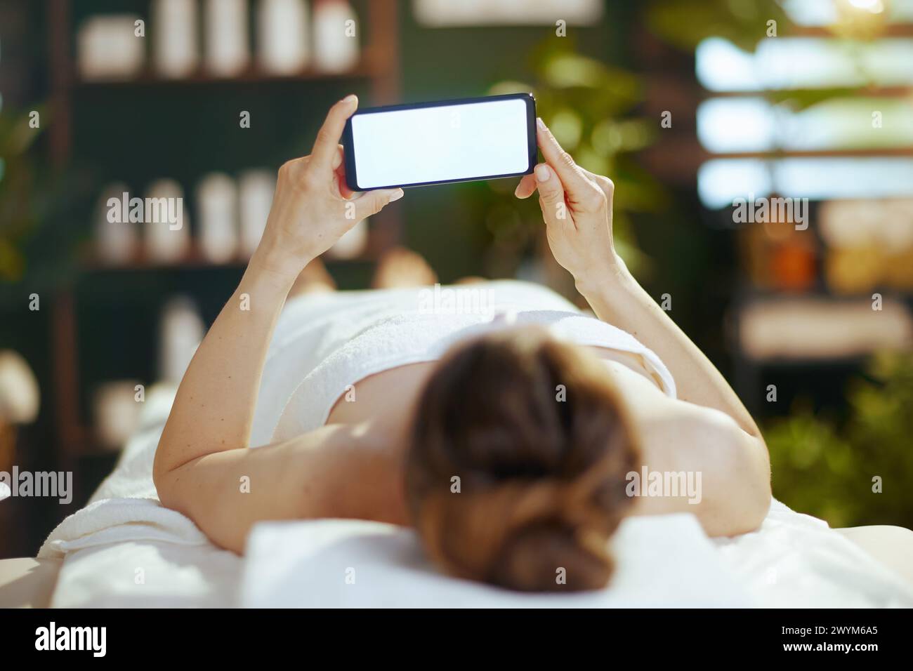Temps de soins. femme moderne détendue dans le salon de spa avec téléphone portable à écran blanc posé sur la table de massage. Banque D'Images