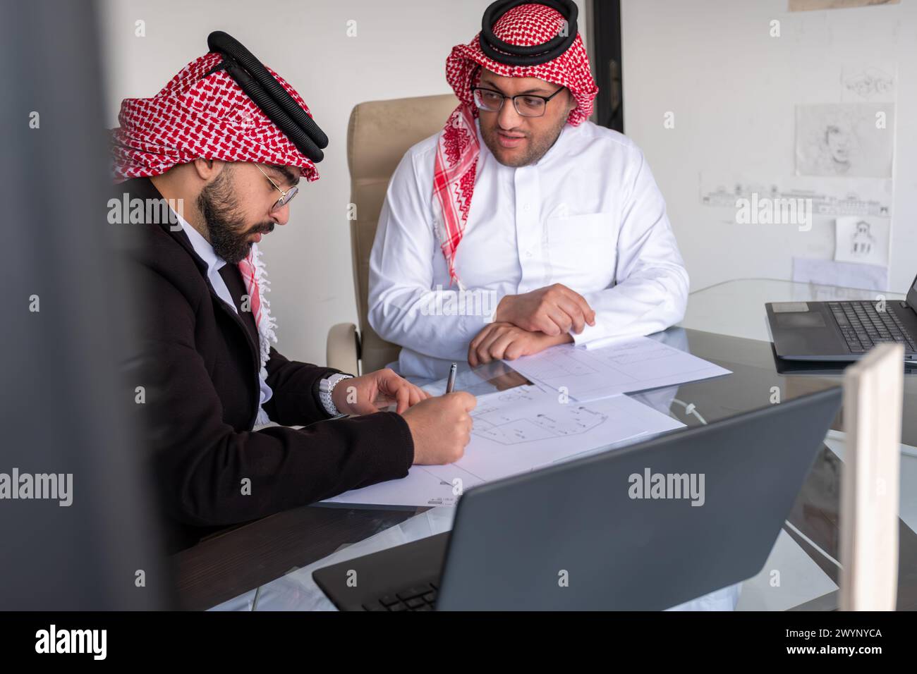 hommes arabes travaillant sur le projet en utilisant un ordinateur portable et des papiers tout en parlant et en vérifiant toutes les possibilités pour améliorer les résultats Banque D'Images