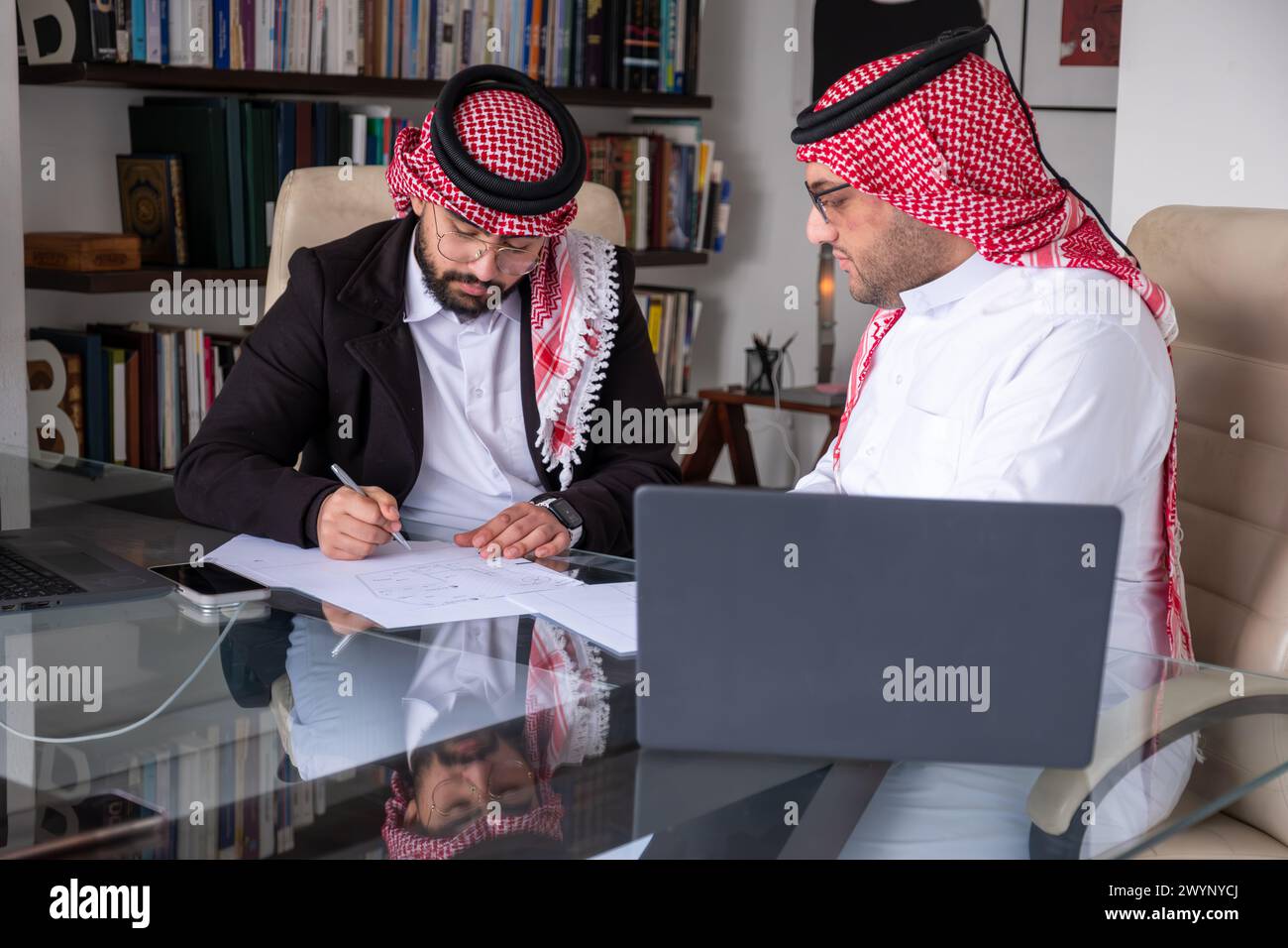 hommes arabes travaillant sur le projet en utilisant un ordinateur portable et des papiers tout en parlant et en vérifiant toutes les possibilités pour améliorer les résultats Banque D'Images