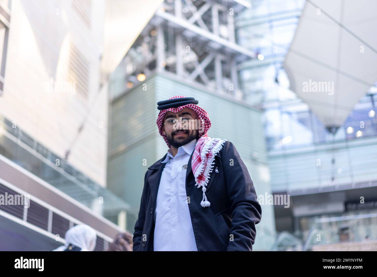Dans un paysage urbain élégant et moderne, un jeune homme d'affaires arabe se tient confiant, entouré de voitures de luxe et de gratte-ciel imposants Banque D'Images