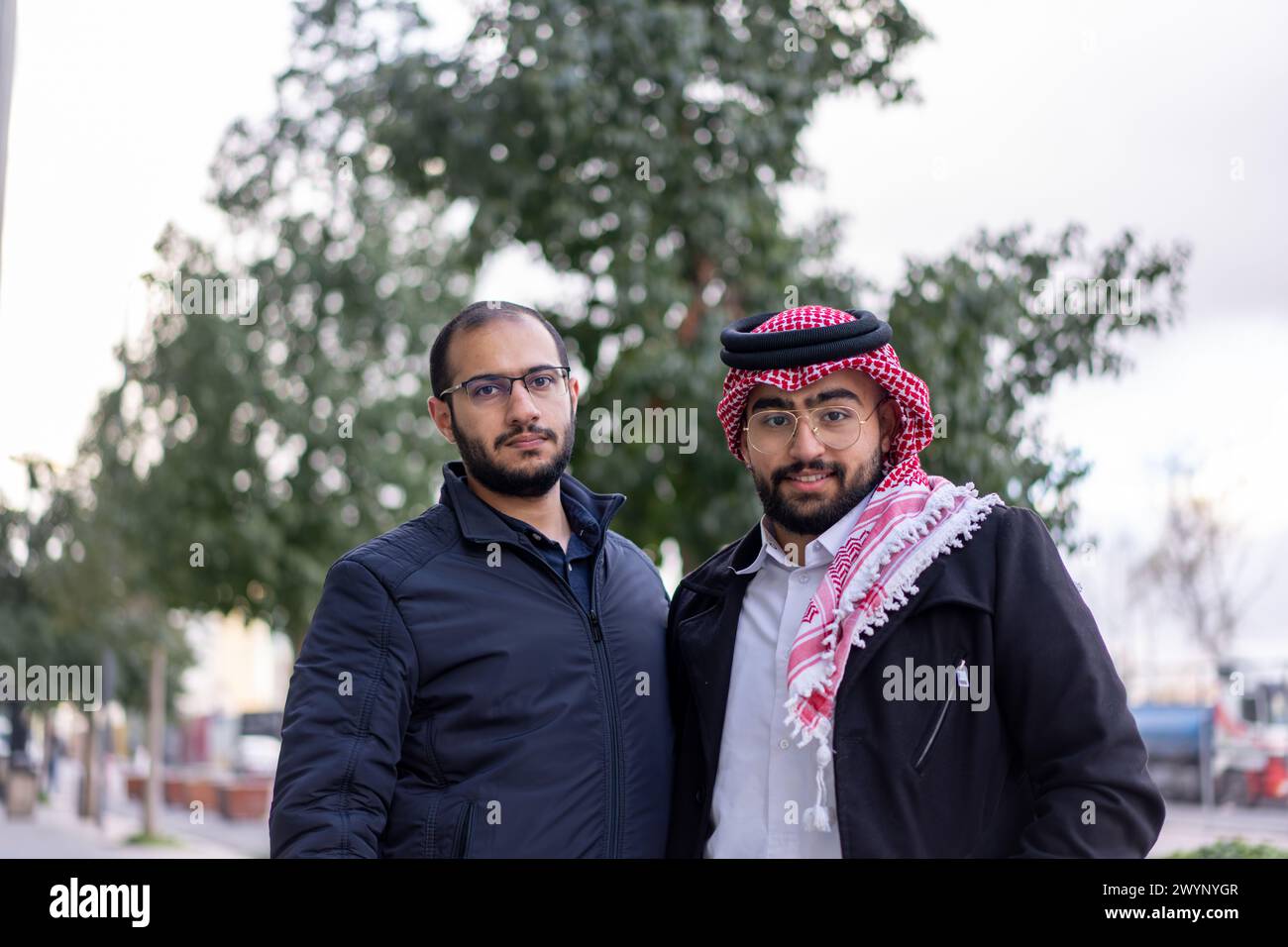 Dans un paysage urbain élégant et moderne, un jeune homme d'affaires arabe se tient confiant, entouré de voitures de luxe et de gratte-ciel imposants Banque D'Images