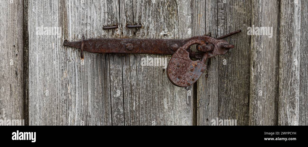 Vue rapprochée de l'ancien cadenas rouillé sur une porte en bois gris vieilli. Banque D'Images