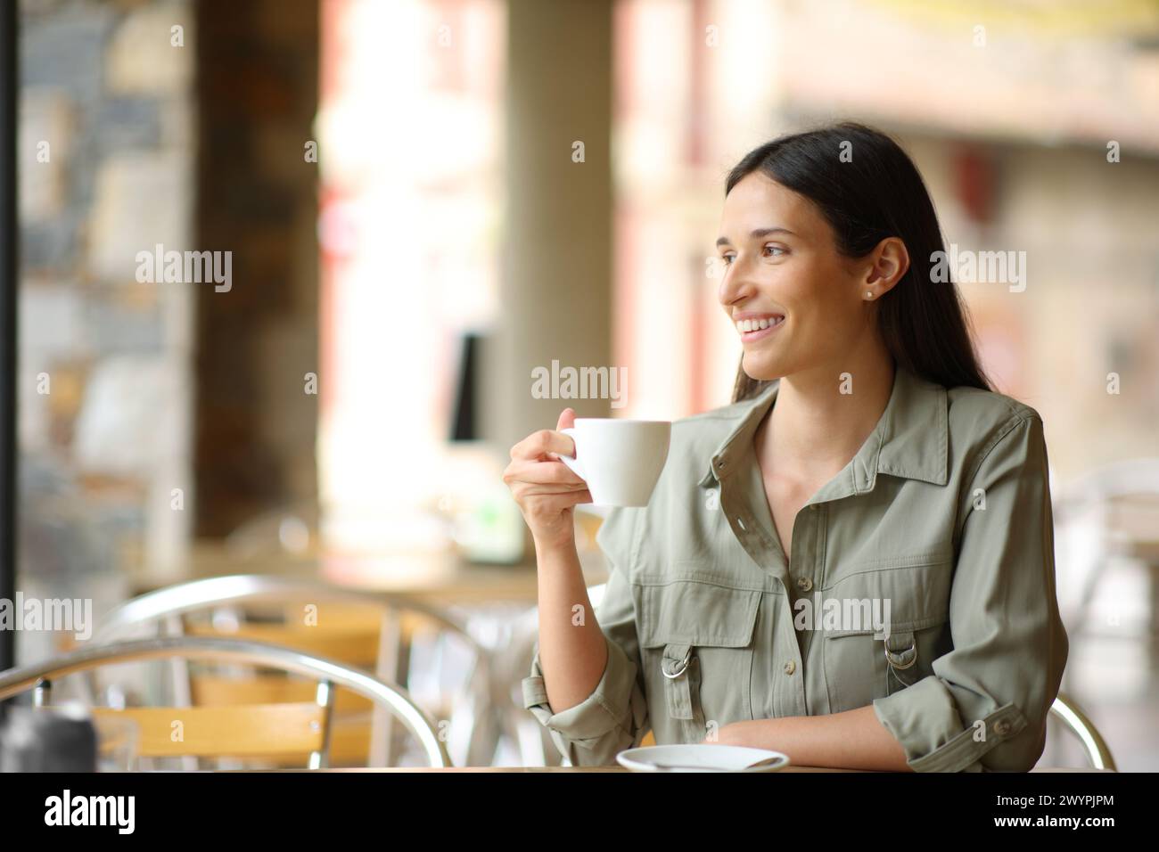 Femme heureuse assise dans un café buvant contempler Banque D'Images