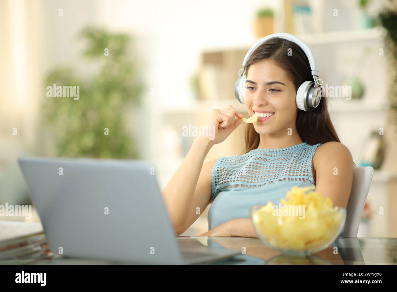 Femme heureuse mangeant une collation et regardant un film sur ordinateur portable à la maison Banque D'Images