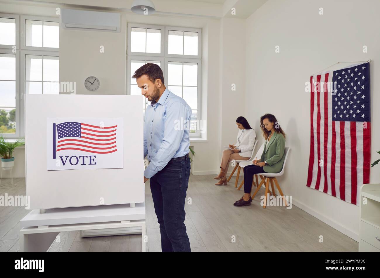 Jeune homme électeur américain debout au centre de vote dans le kiosque de vote faisant un choix le jour de l'élection. Banque D'Images
