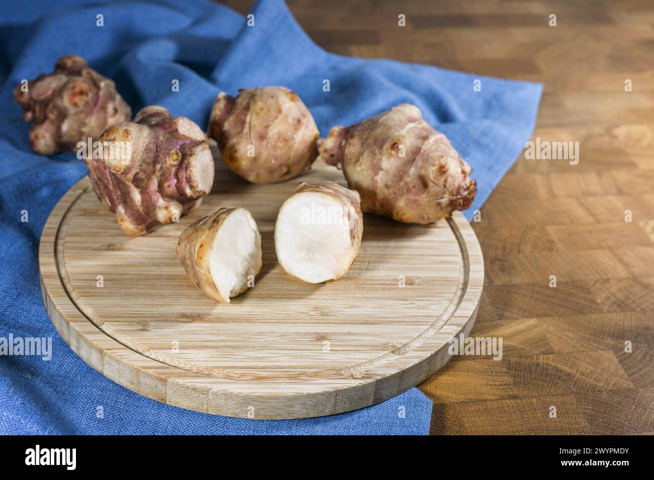 Légume racine d'artichaut de Jérusalem ou topinambur (Helianthus tuberosus), entier et coupé en deux sur une planche de cuisine en bois rustique et une serviette bleue, pour la guérison Banque D'Images