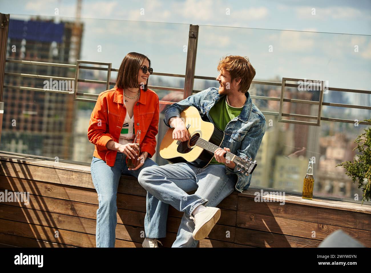 Un homme et une femme sont assis sur un banc, tapant des guitares alors qu'ils s'harmonisent dans un cadre extérieur serein Banque D'Images