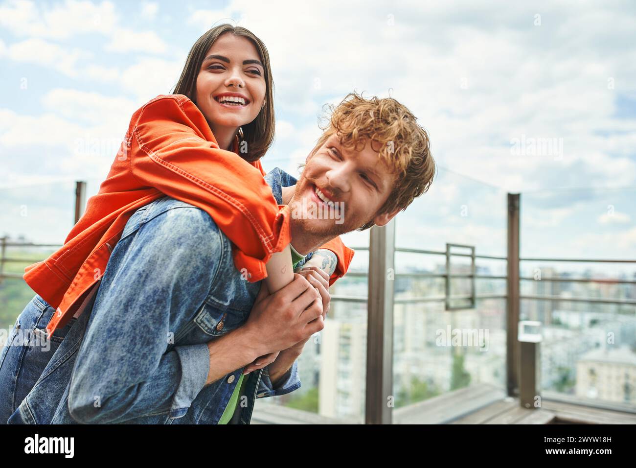 Un homme courageux tient une femme debout sur le bord d'un grand bâtiment, surplombant la ville en contrebas, montrant l'amour et la confiance Banque D'Images