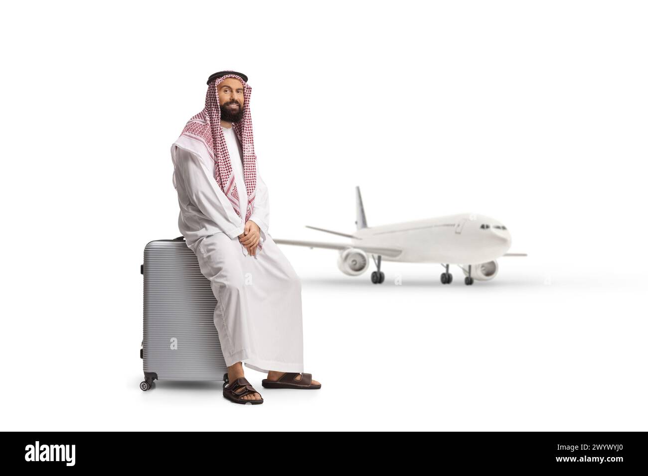 Homme arabe saoudien assis sur une valise à l'aéroport et attendant un avion isolé sur fond blanc, Banque D'Images