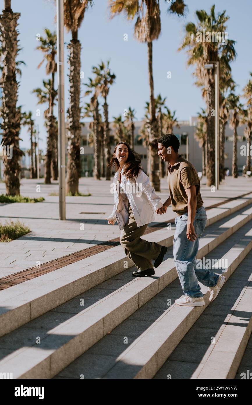 Les jeunes couples se réunissent joyeusement sur les marches d'une promenade bordée de palmiers dans le paysage urbain animé de Barcelonas Banque D'Images