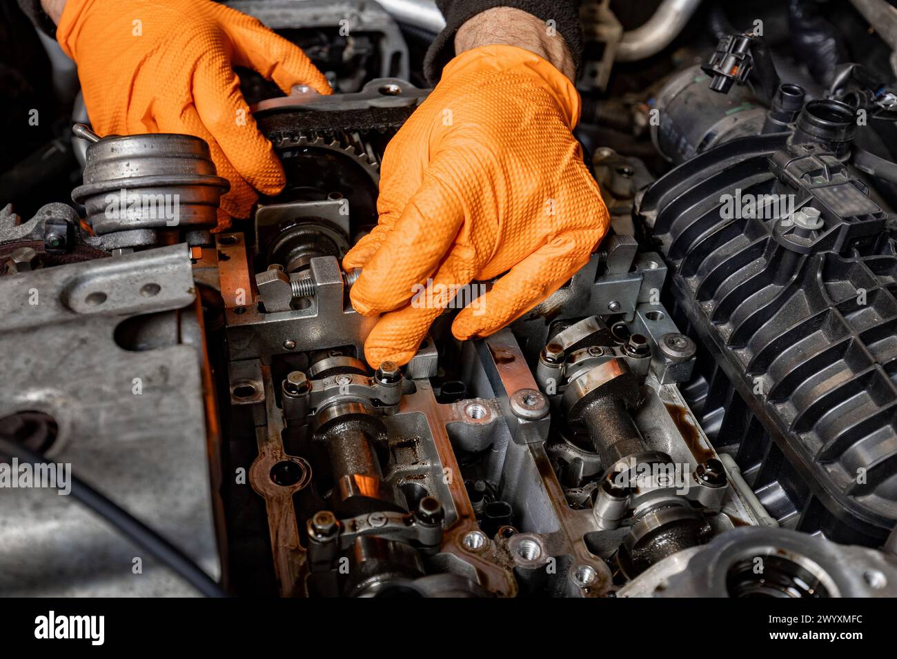 Vue détaillée des mains d'un mécanicien automobile, protégées par des gants orange, alors qu'ils travaillent attentivement à la réparation d'un moteur de voiture ouvert dans un service automobile Banque D'Images