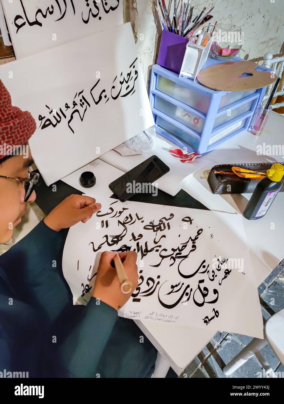 Un garçon plus jeune dessine la calligraphie arabe, de gros plan les mains d'un garçon musulman écrivant du texte arabe avec des stylos en bambou et de l'encre noire sur du papier Banque D'Images