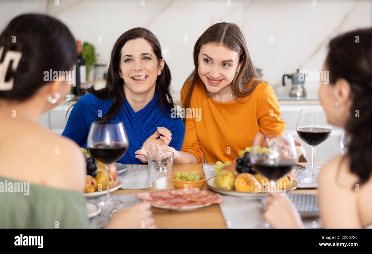 Des femmes heureuses se sont rassemblées autour d’une table festive, participant à des discussions animées et profitant des délices du vin Banque D'Images