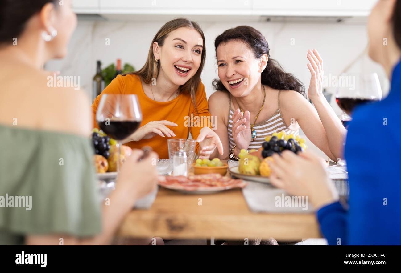 Des femmes heureuses se sont rassemblées autour d’une table festive, participant à des discussions animées et profitant des délices du vin Banque D'Images