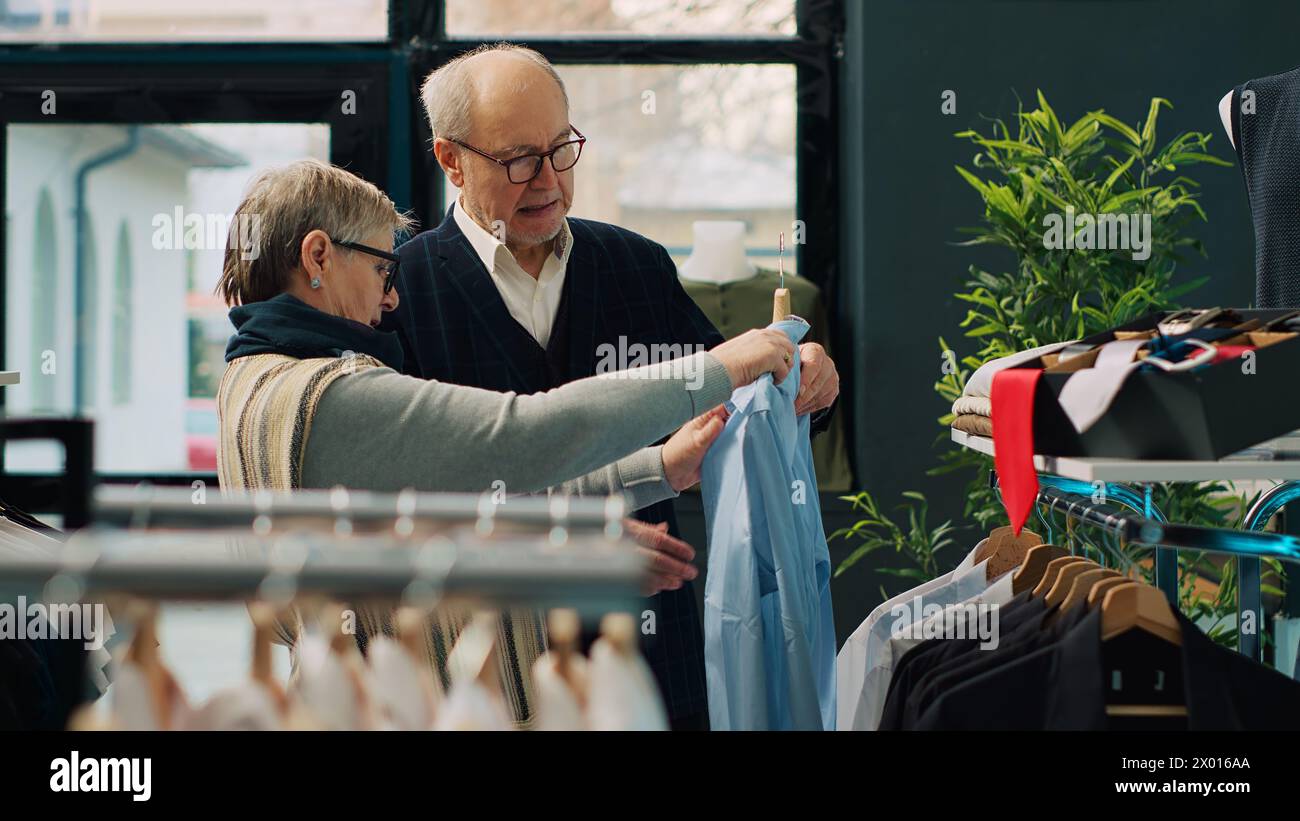 Couple senior shopping pour des vêtements d'extérieur formels à la boutique de mode, à la recherche d'articles de vêtements élégants à la mode pour créer de nouvelles tenues pour homme âgé. Les gens à la recherche de marchandises élégantes. Caméra A. Banque D'Images