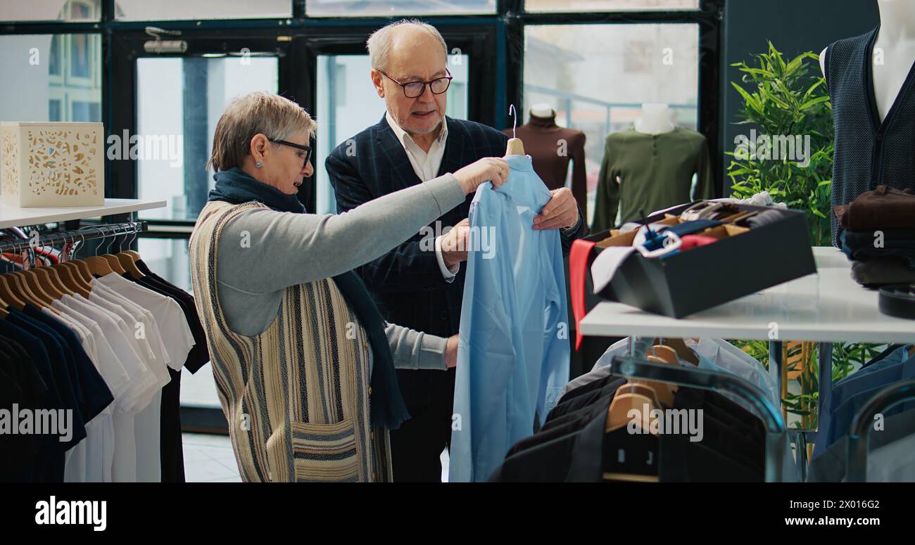 Couple senior shopping pour des vêtements d'extérieur formels à la boutique de mode, à la recherche d'articles de vêtements élégants à la mode pour créer de nouvelles tenues pour homme âgé. Les gens à la recherche de marchandises élégantes. Caméra B. Banque D'Images