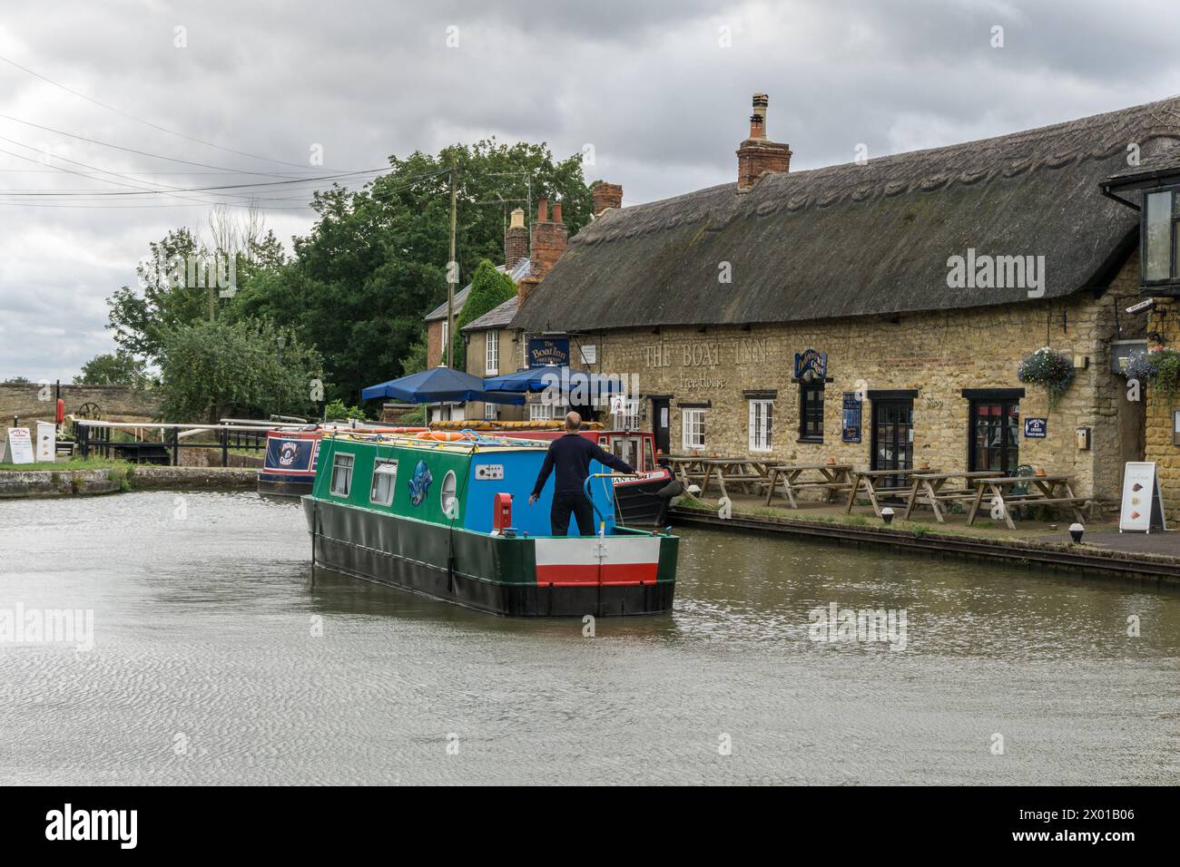 Bateau étroit naviguant sur le canal de Grand Union avec le Boat Inn en arrière-plan, Stoke Bruerne, Northamptonshire, Royaume-Uni Banque D'Images