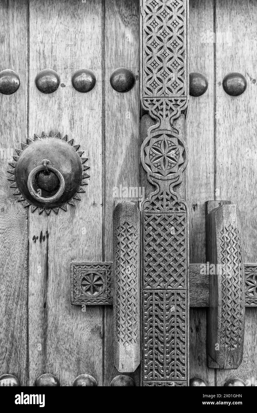 Une image monochrome montrant le détail d'une porte en bois sculpté, poignée et serrure à l'entrée d'une maison arabe traditionnelle restaurée. Banque D'Images