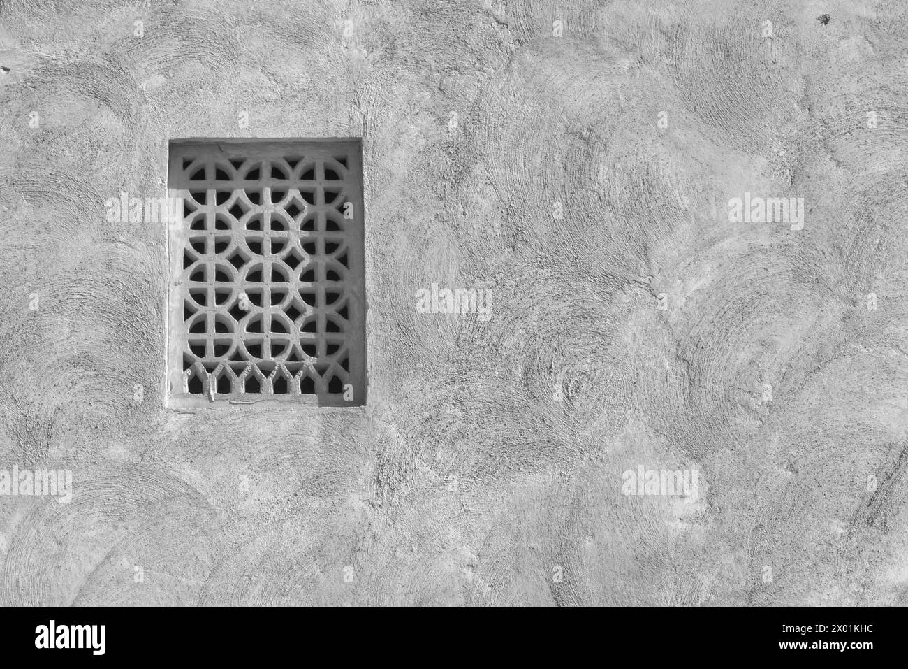 Monochrome, image filtrée d'un treillis de ventilation en plâtre dans le mur extérieur en adobe d'une maison arabe traditionnelle. Banque D'Images