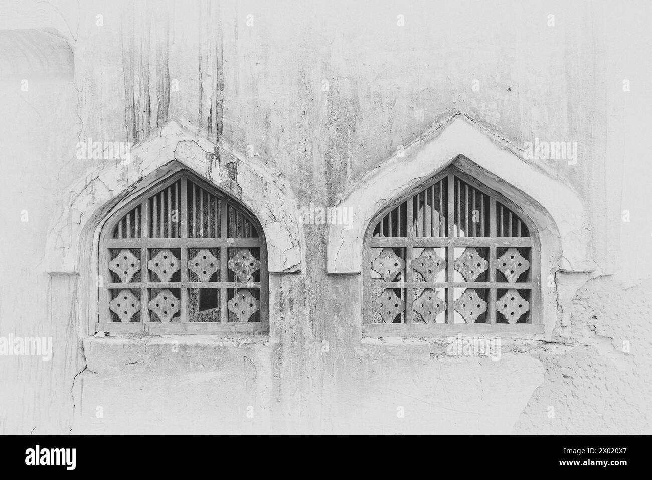 Une image monochrome, filtrée et vignettée de deux fenêtres cintrées en ogée avec des treillis en bois dans le mur d'un bâtiment abandonné et abandonné dans le Middl Banque D'Images