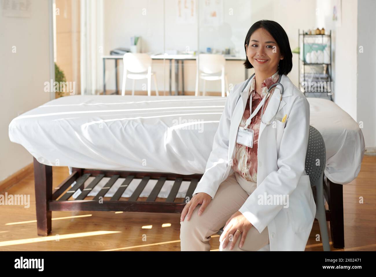 Médecin généraliste souriant assis devant le lit d'hôpital dans le service Banque D'Images